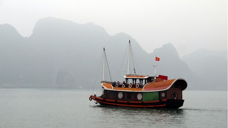Traditional junk boat cruising Lan Ha Bay on a foggy day in March 2019